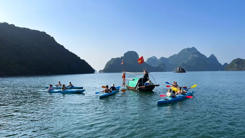 Kayakers paddle around a small wooden boat among limestone islands in Lan Ha Bay near Cat Ba.