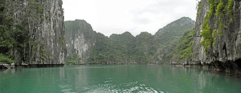 Limestone karsts rise around a calm turquoise lagoon in Ha Long Bay.