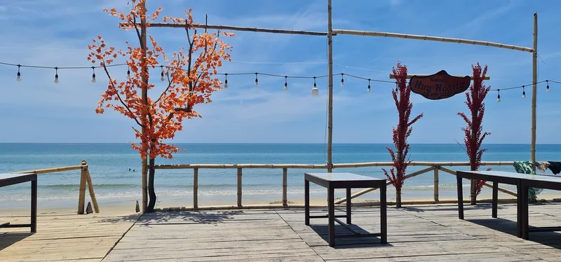 A bamboo beach deck with red flowering trees and string lights overlooks turquoise sea along the Hue to Hoi An coast.