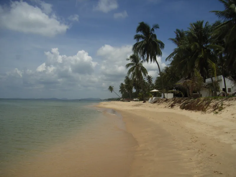 A quiet sandy beach lined with coconut palms and small bungalows on Phu Quoc island.