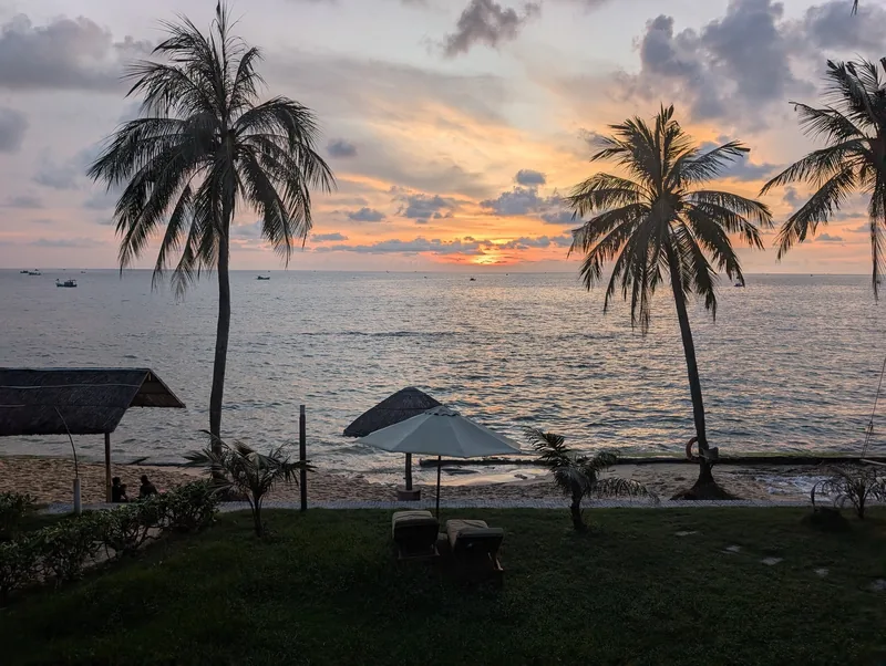 Palm trees frame a golden sunset over the sea from a beach resort in Phu Quoc.