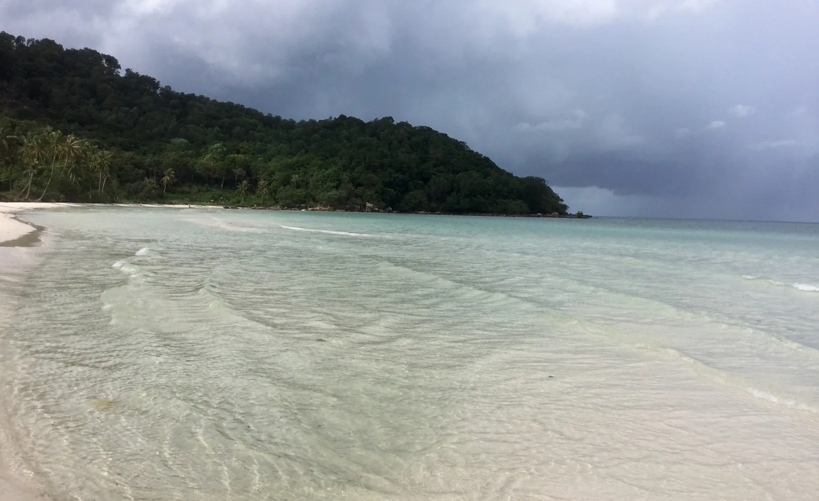 Storm clouds gather over the forested headland and calm turquoise shallows of Bai Sao beach in Phu Quoc.