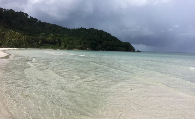 Storm clouds gather over the forested headland and calm turquoise shallows of Bai Sao beach in Phu Quoc.